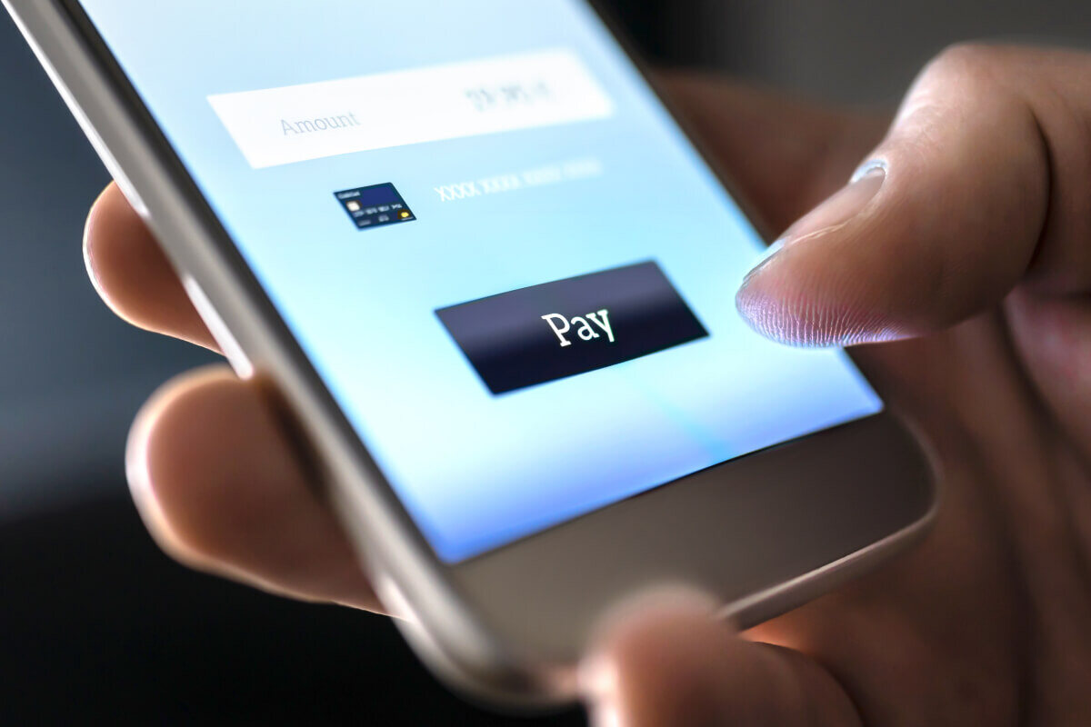 Extreme close-up of a hand holding a smartphone while a text to pay mobile payment is completed. The person's thumb hovers over the "Pay" button to complete the transaction.