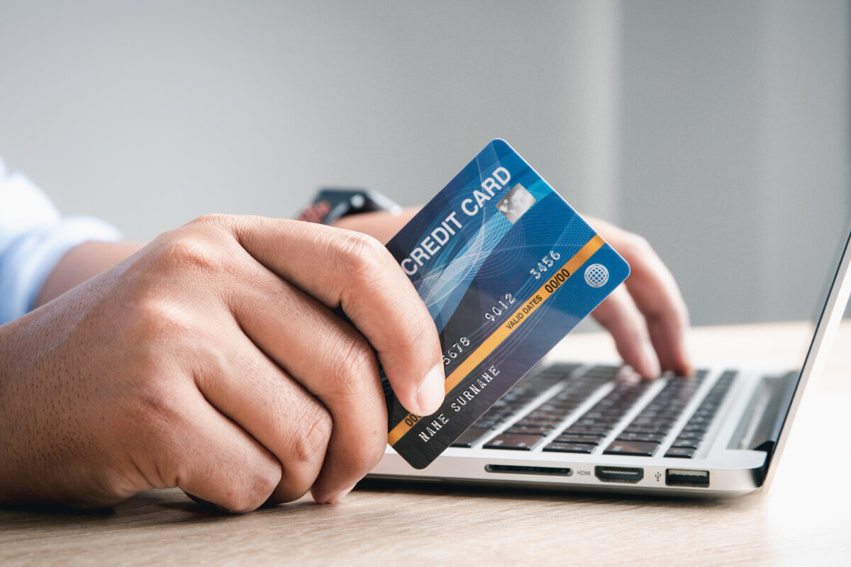 Close up of a man's hands while he holds a credit card next to his open laptop, completing a virtual payment online.